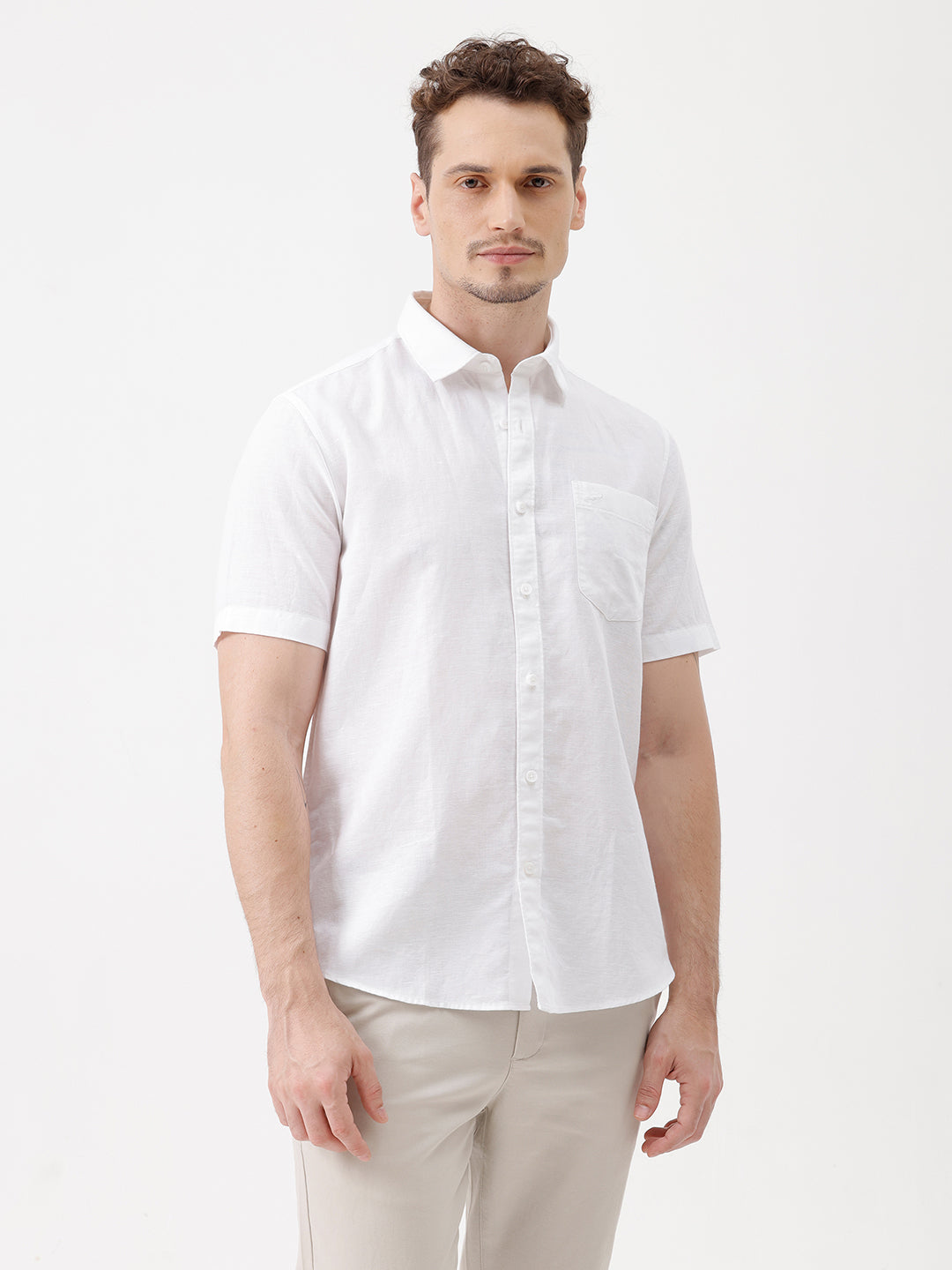 A man wearing a white short-sleeve button-up shirt with a chest pocket and beige trousers, standing against a plain white studio background.