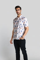 Man wearing a patterned shirt and black pants on a plain background