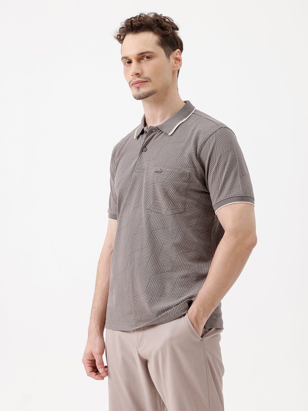A man wearing a short-sleeve polo shirt with a gray and white geometric pattern, paired with beige trousers, standing against a plain white studio background.