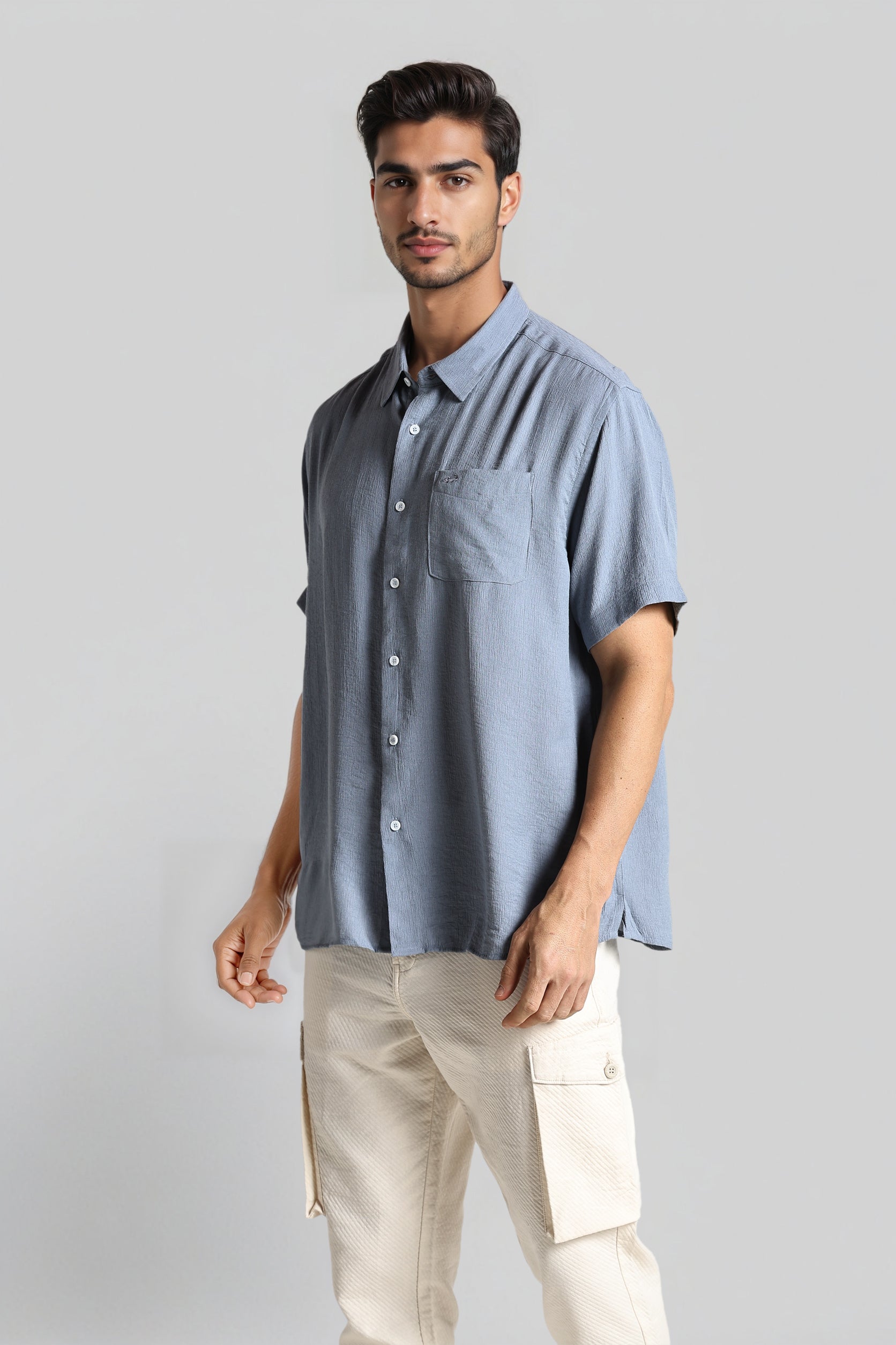 Man wearing a light blue button-up shirt and beige pants on a gray background