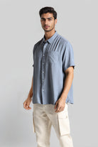 Man wearing a light blue button-up shirt and beige pants on a gray background