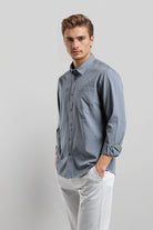 Man wearing a light blue button-up shirt and white pants on a gray background