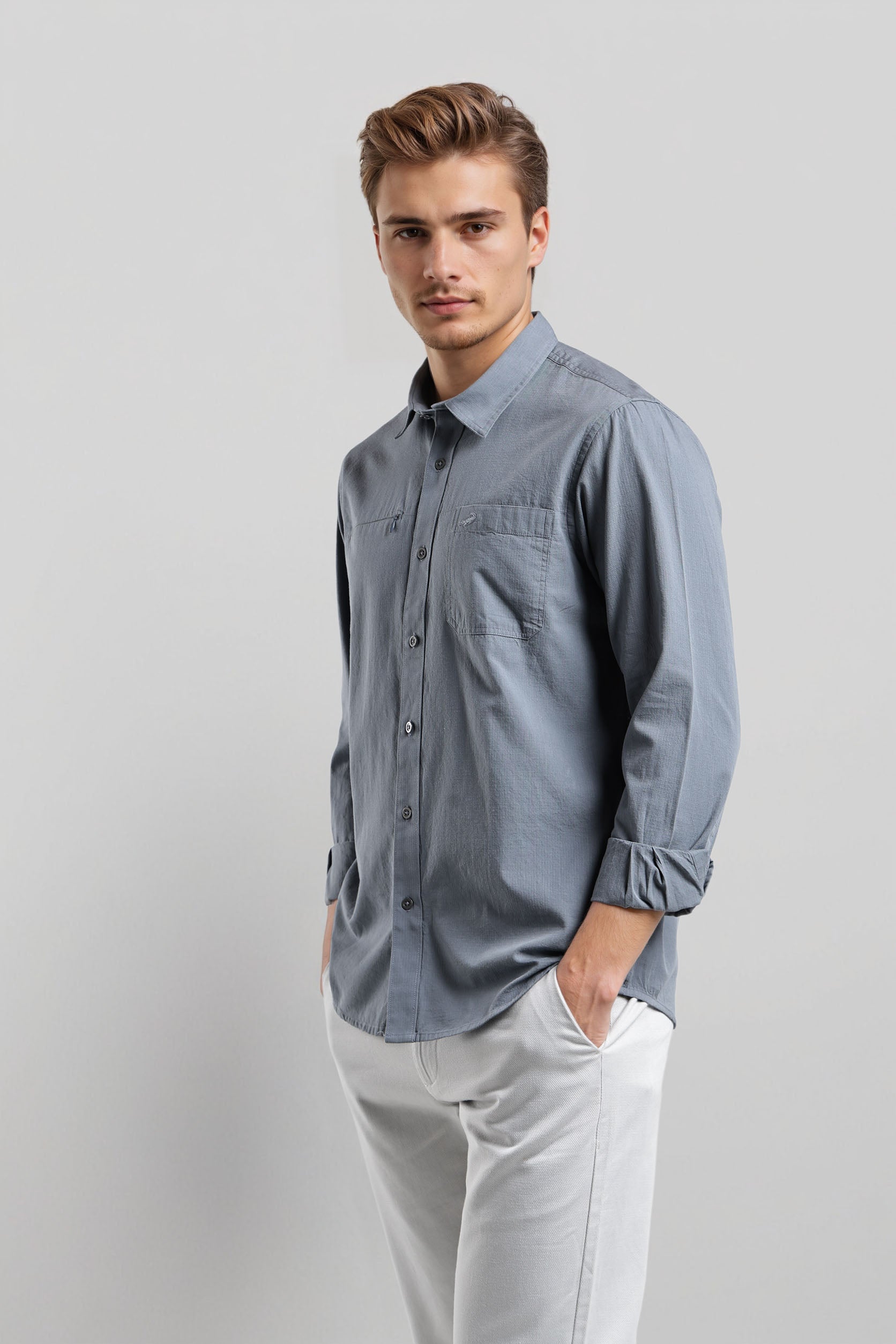 Man wearing a light blue button-up shirt and white pants on a gray background