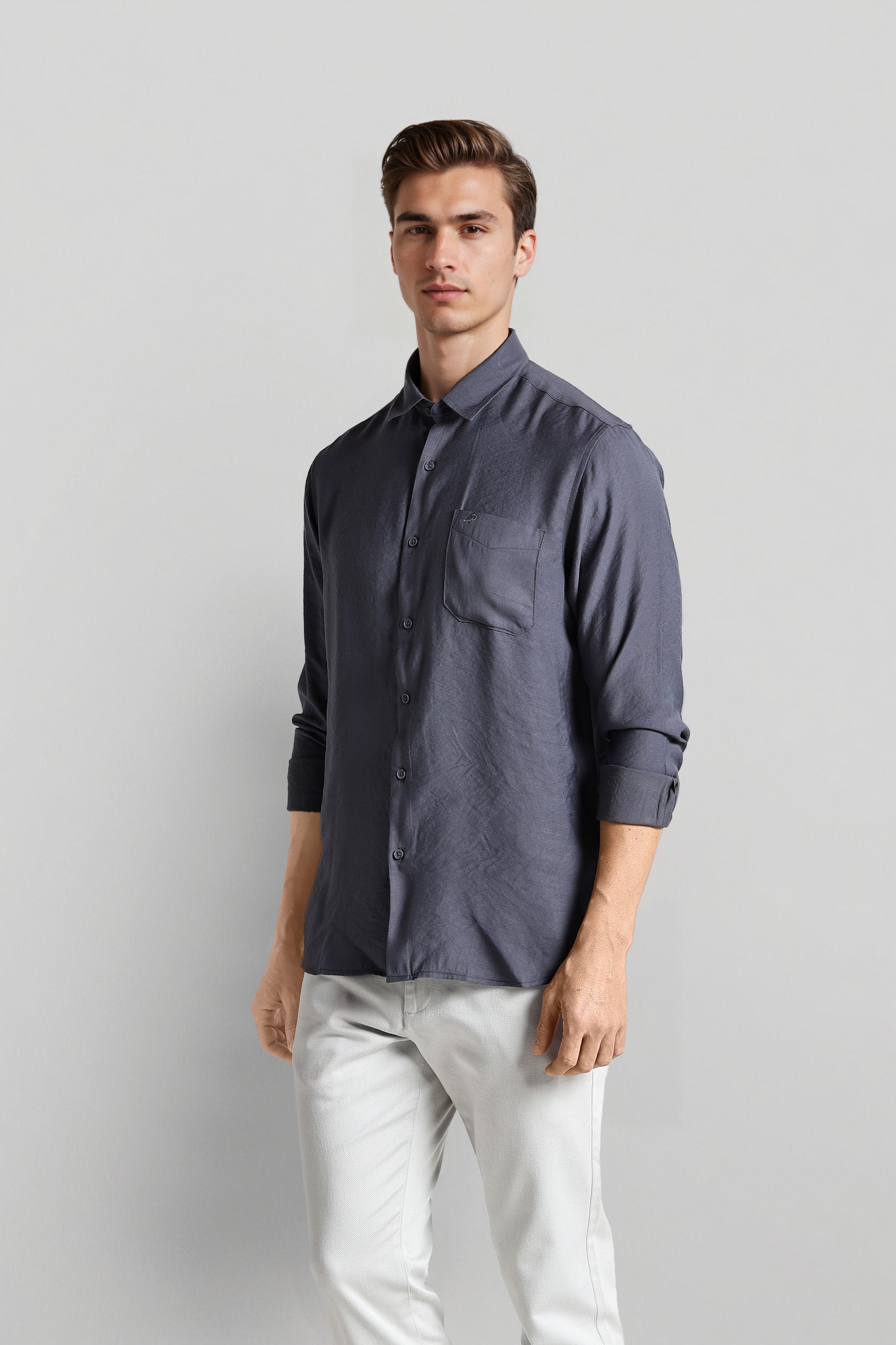 Man wearing a dark gray shirt and light-colored pants against a plain background