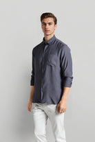 Man wearing a dark gray shirt and light-colored pants against a plain background