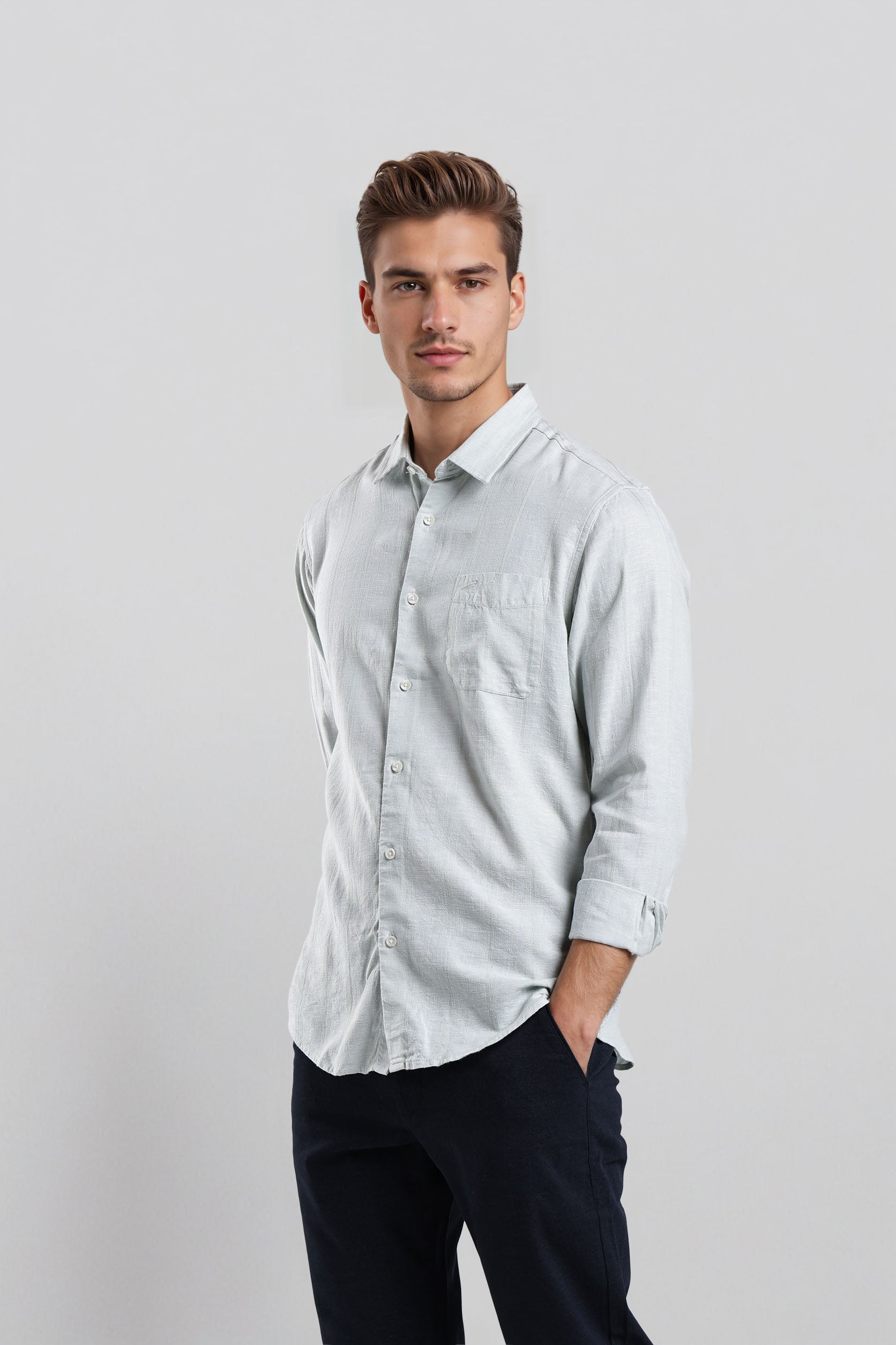 Man wearing a light gray button-up shirt and dark pants on a white background