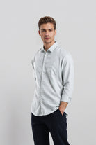 Man wearing a light gray button-up shirt and dark pants on a white background