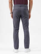 A person wearing slim-fit charcoal gray chino pants, paired with a dark purple shirt and white sneakers, standing against a plain white studio background.