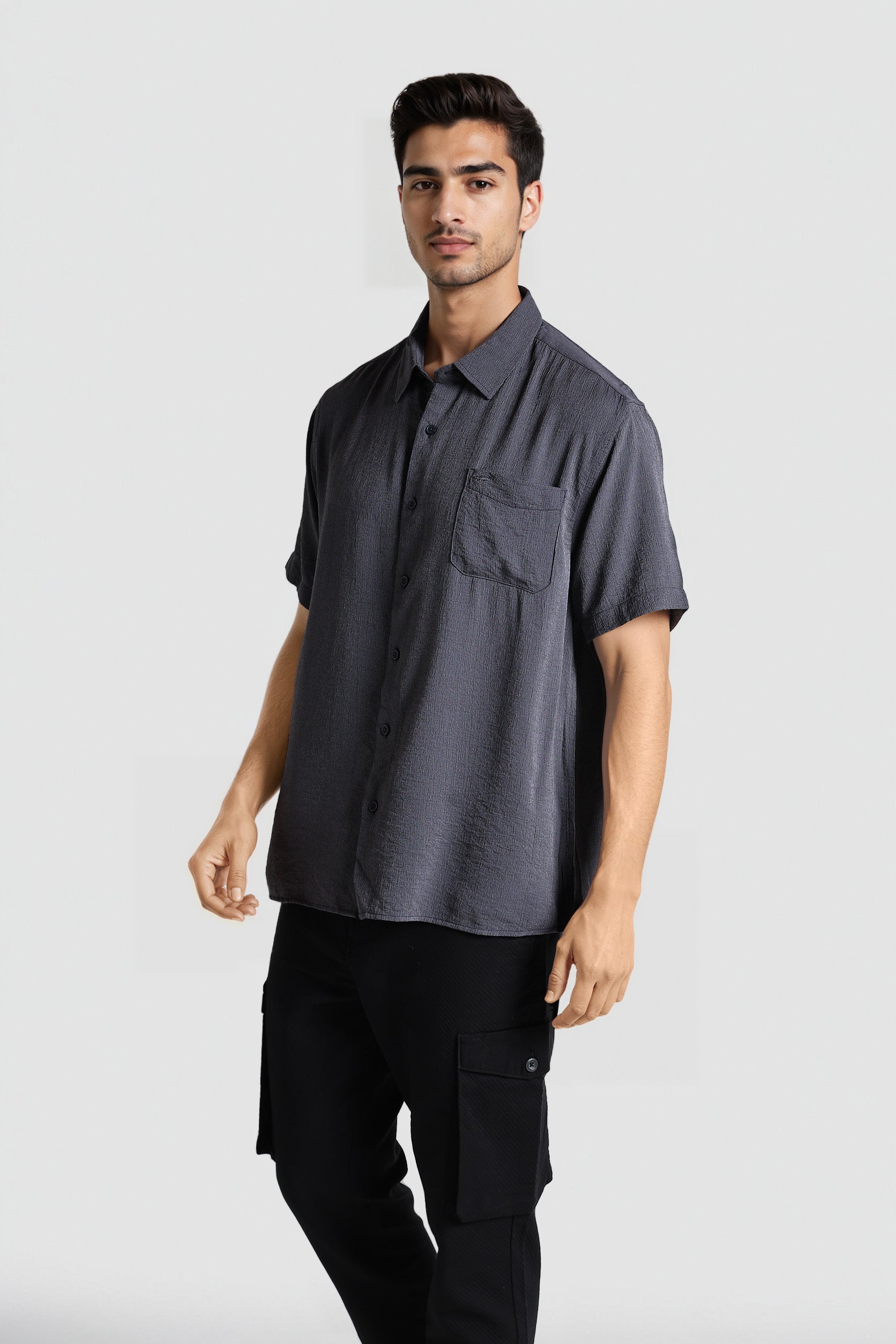 Man wearing a dark gray short-sleeve shirt and black pants on a light gray background