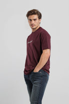 Man wearing a maroon t-shirt with a logo on a light gray background