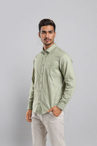 Man wearing a light green shirt and white pants against a gray background