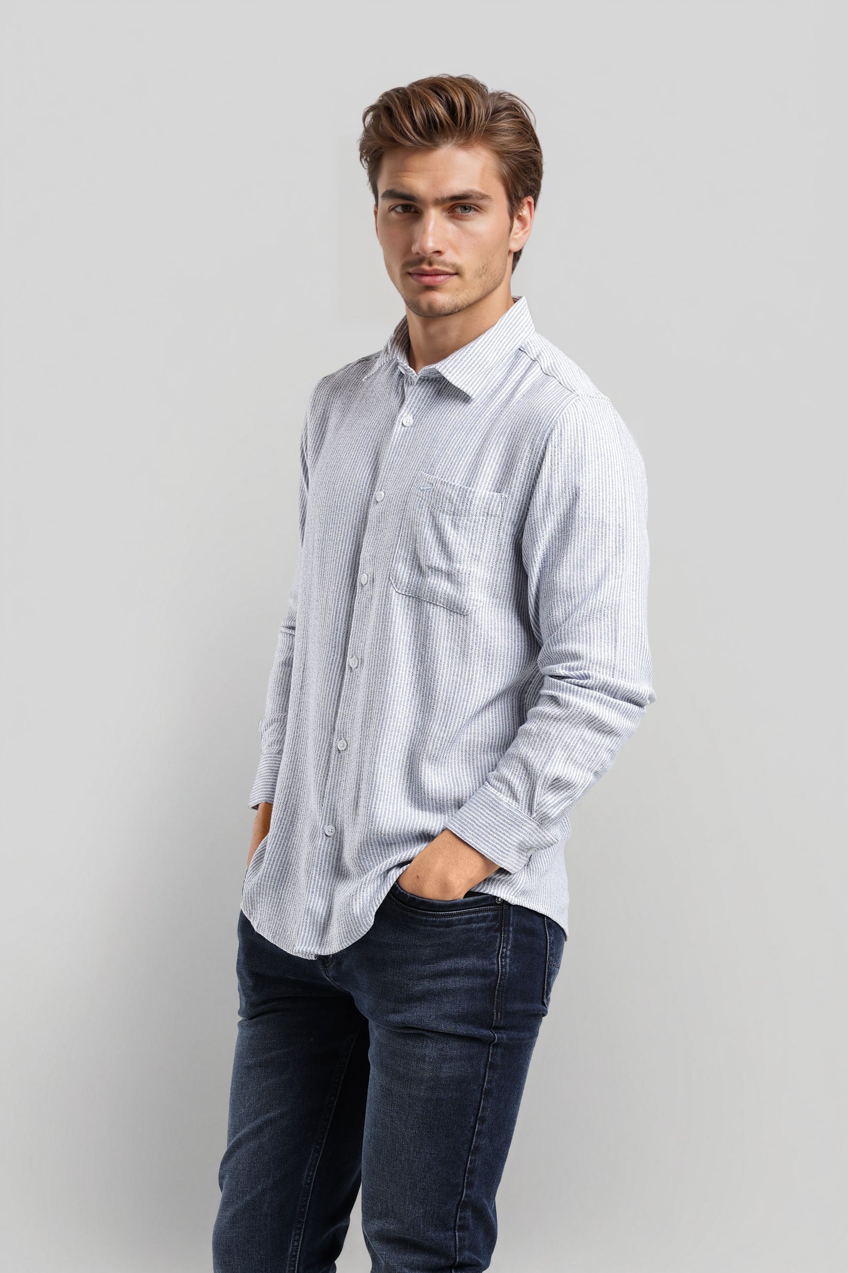 Man wearing a light blue striped shirt and dark jeans against a plain background