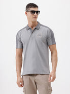 A man wearing a light gray short-sleeve polo shirt with darker gray shoulder panels and a small crest logo on the left chest, paired with khaki cargo pants, against a plain light gray studio background.