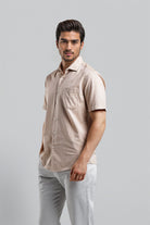 Man wearing a beige shirt and white pants against a gray background