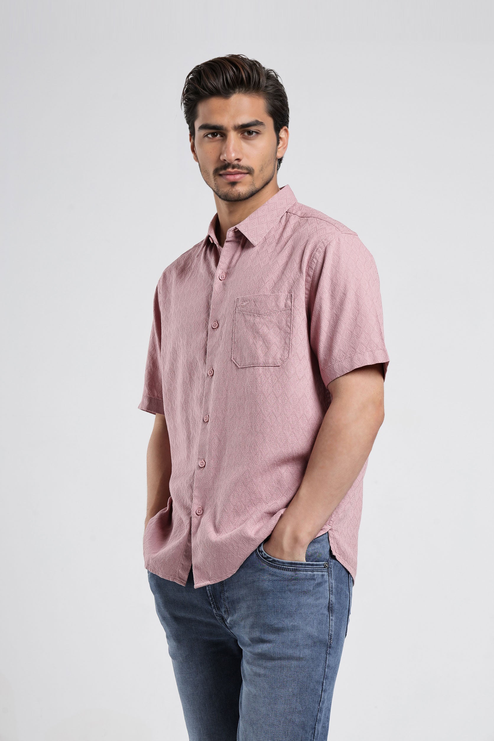 Man wearing a pink short-sleeve shirt and blue jeans on a white background