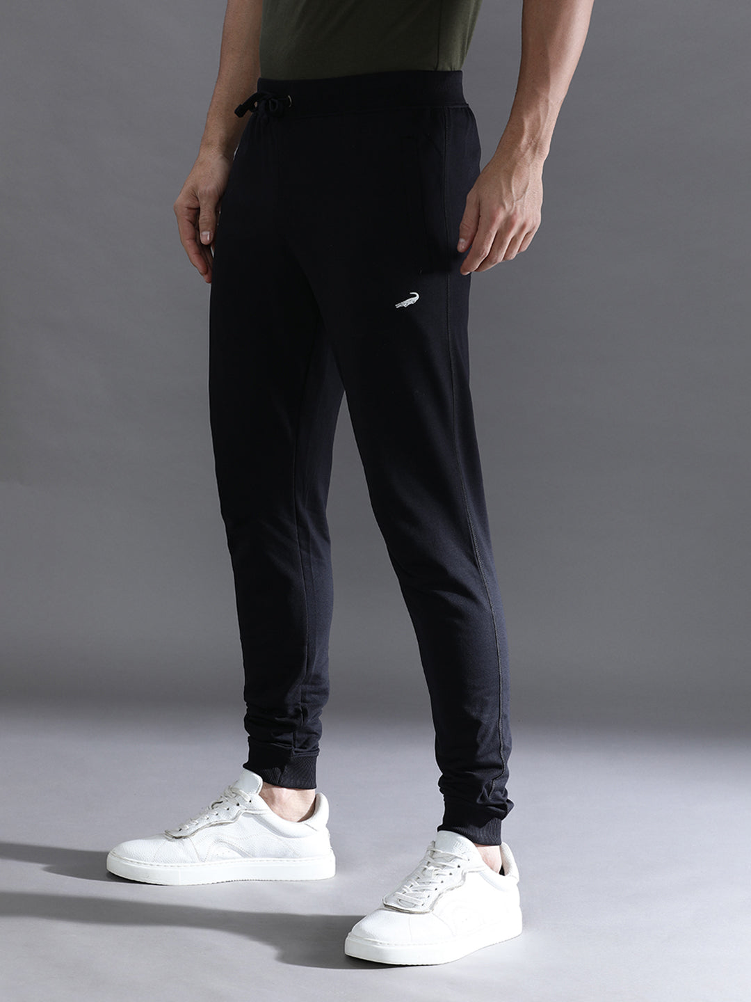 Person wearing black jogger pants and white sneakers on a gray background