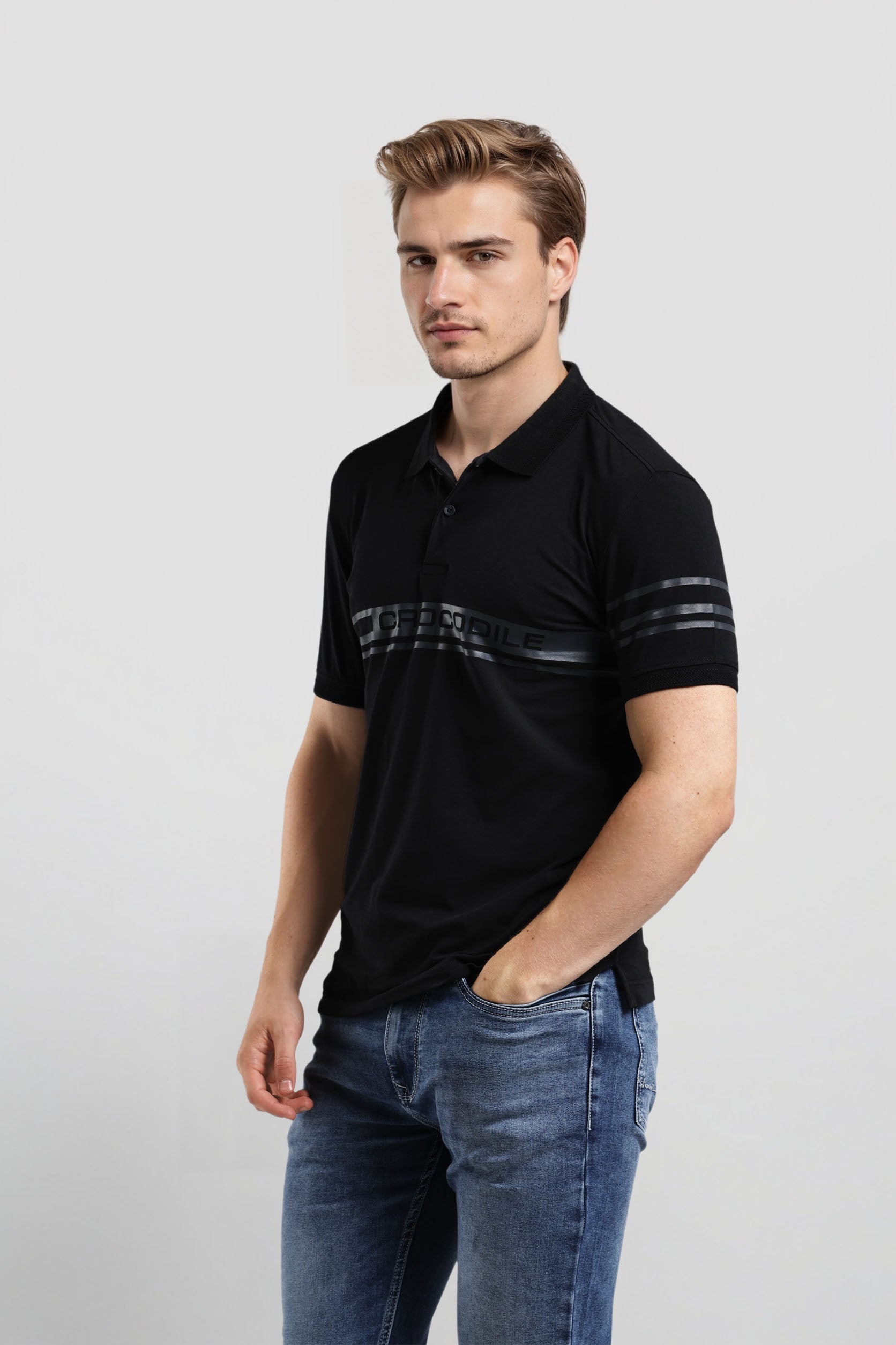 Man wearing a black polo shirt with white text and blue jeans on a light gray background