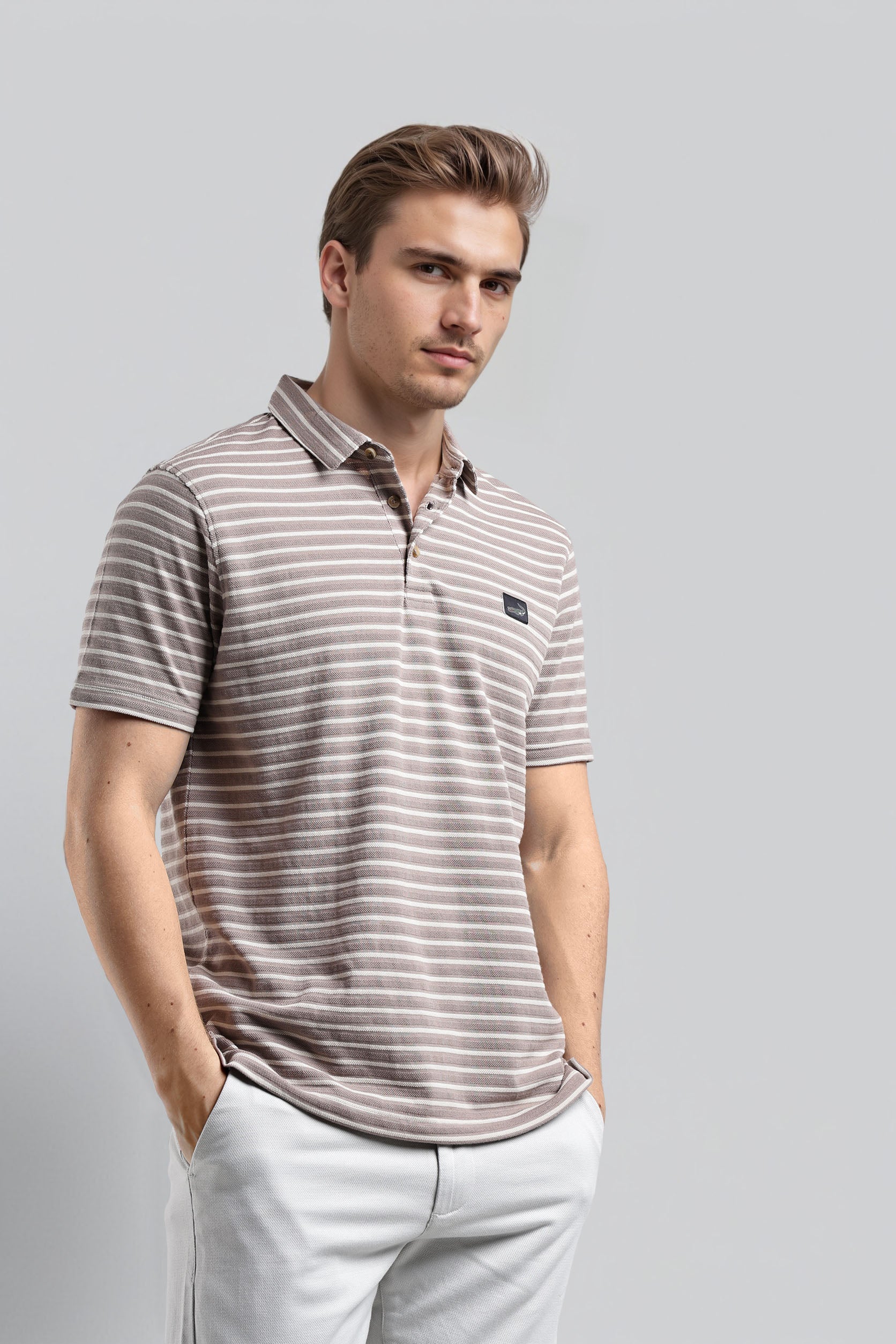 Man wearing a striped polo shirt and light pants on a gray background