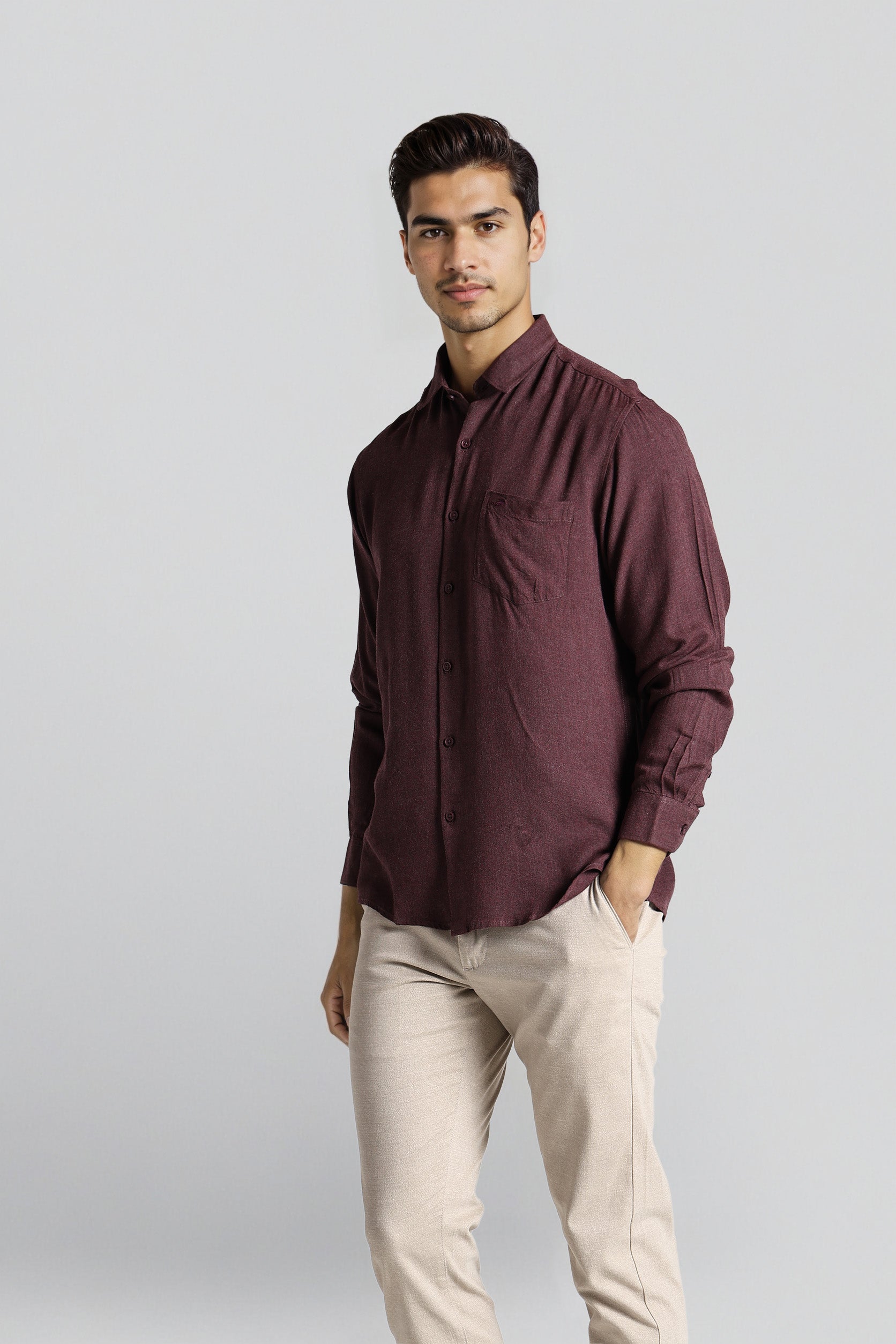 Man wearing a maroon shirt and beige pants on a light gray background