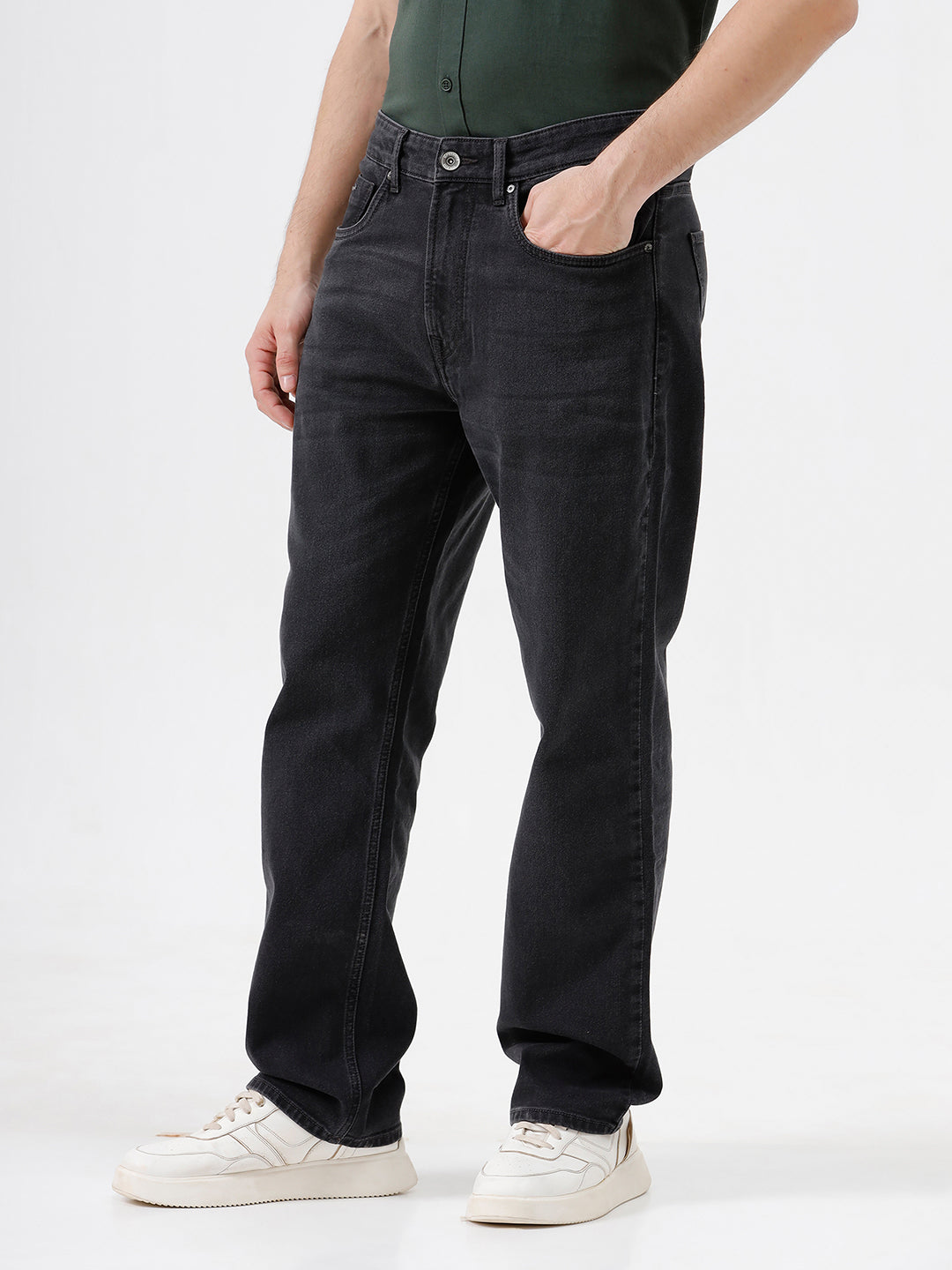 A person wearing dark washed denim jeans, a dark green shirt, and white sneakers, shown from the chest down against a plain light gray studio background.