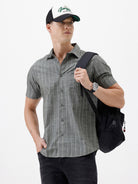 A man wearing a short-sleeve button-up shirt with a gray and white vertical stripe pattern, paired with black pants, standing against a plain white studio background.