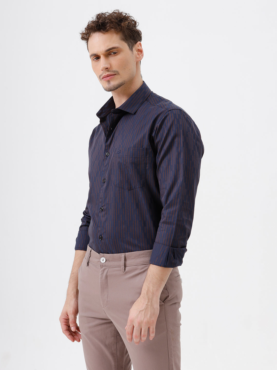 A man wearing a dark navy blue button-down shirt with thin vertical red stripes and light brown trousers, standing against a plain white studio background.