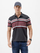 A man wearing a dark gray Lacoste polo shirt with horizontal red and white stripes across the chest and sleeves, paired with blue jeans, against a plain light gray background.