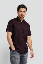 Man wearing a dark brown button-up shirt and gray pants on a white background