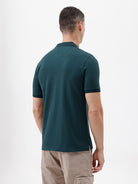 A man wearing a dark teal short-sleeve polo shirt with a chest pocket, paired with beige cargo pants, standing against a plain white studio background.