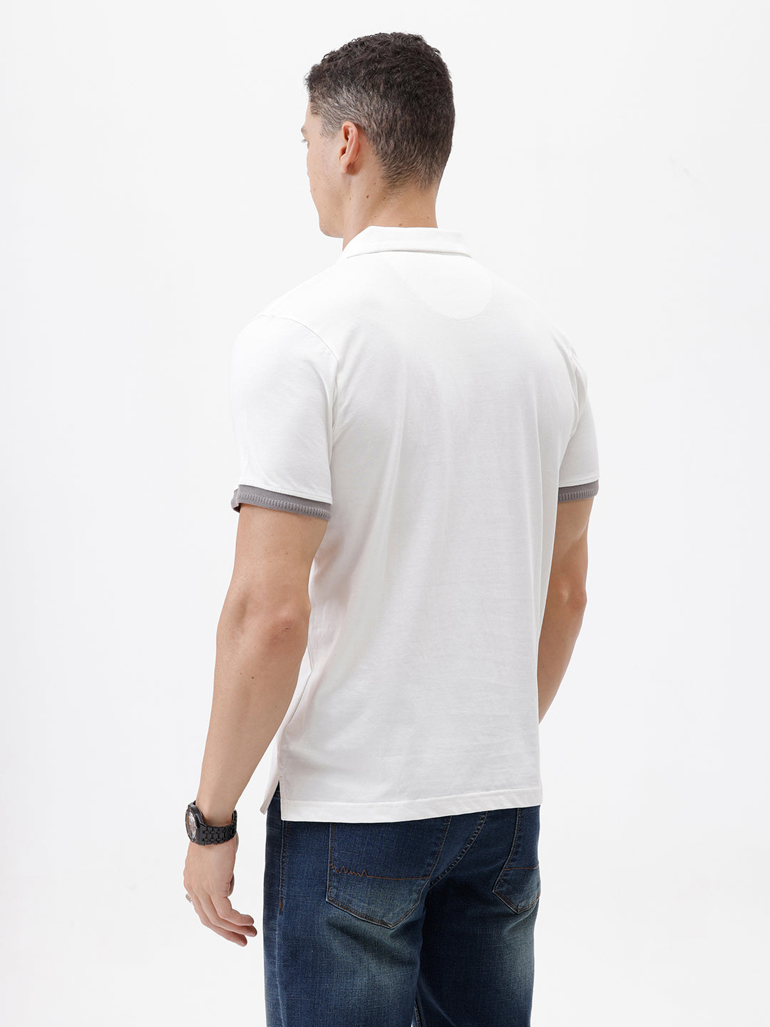 A man wearing a white short-sleeve polo shirt with gray ribbed trim on the collar and sleeve cuffs, paired with dark blue jeans, photographed against a plain white studio background.