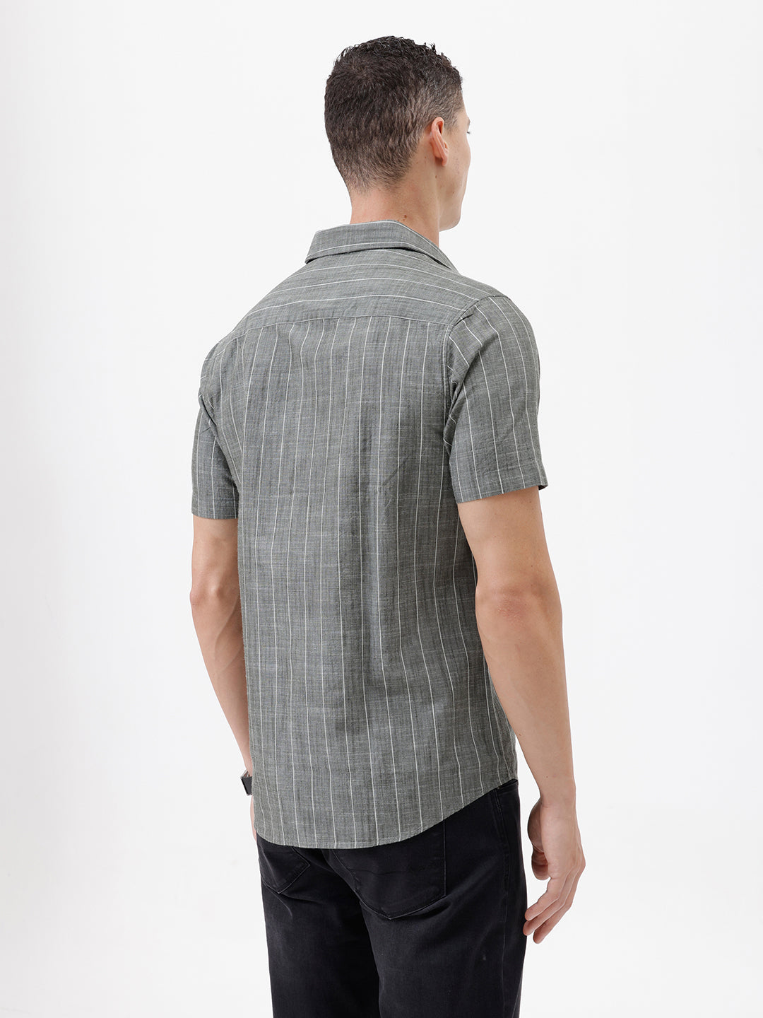 A man wearing a short-sleeve button-up shirt with a gray and white vertical stripe pattern, paired with black pants, standing against a plain white studio background.