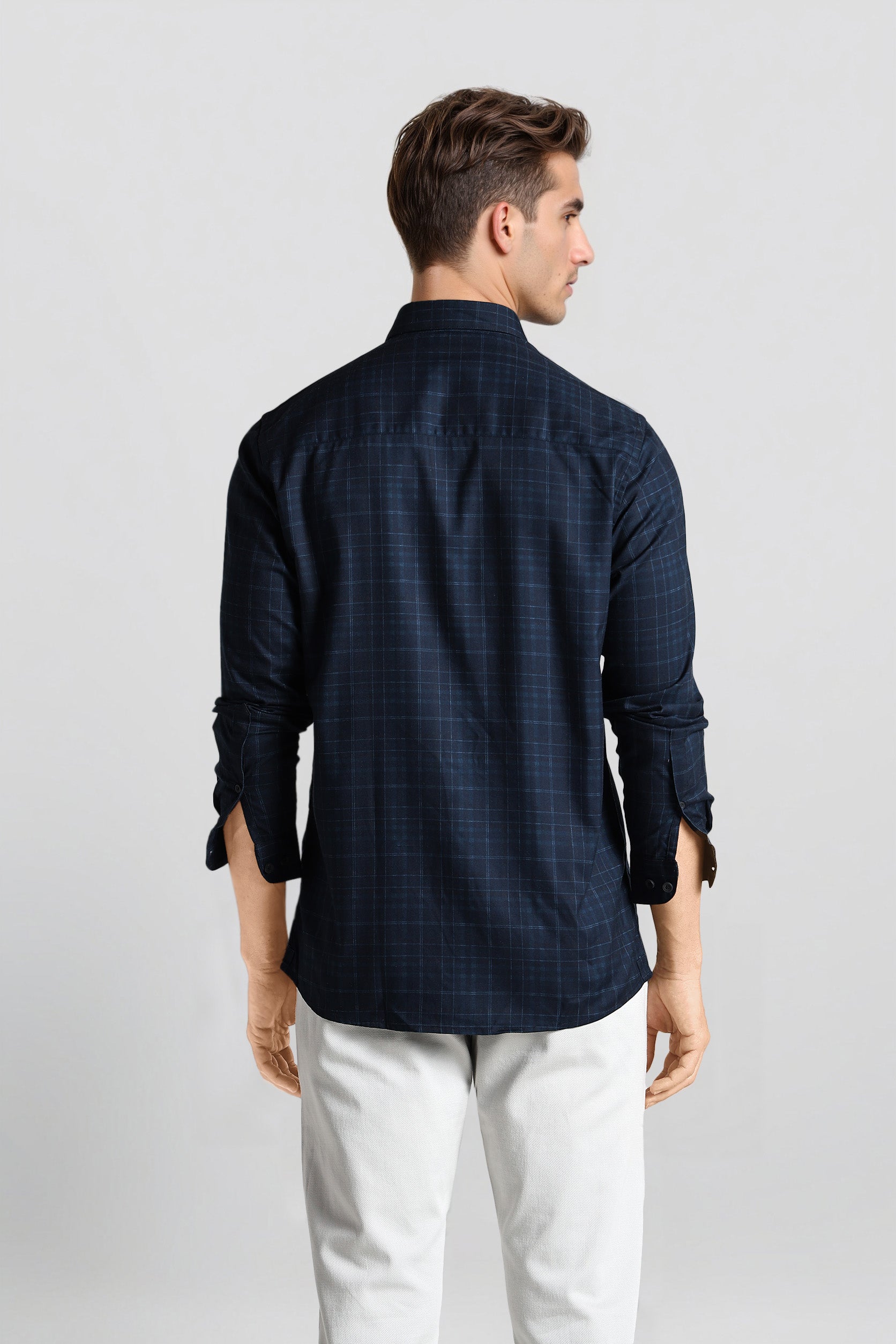 Man wearing a dark blue checkered shirt and white pants on a light gray background