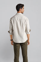 Man wearing a light-colored shirt and dark pants against a plain background