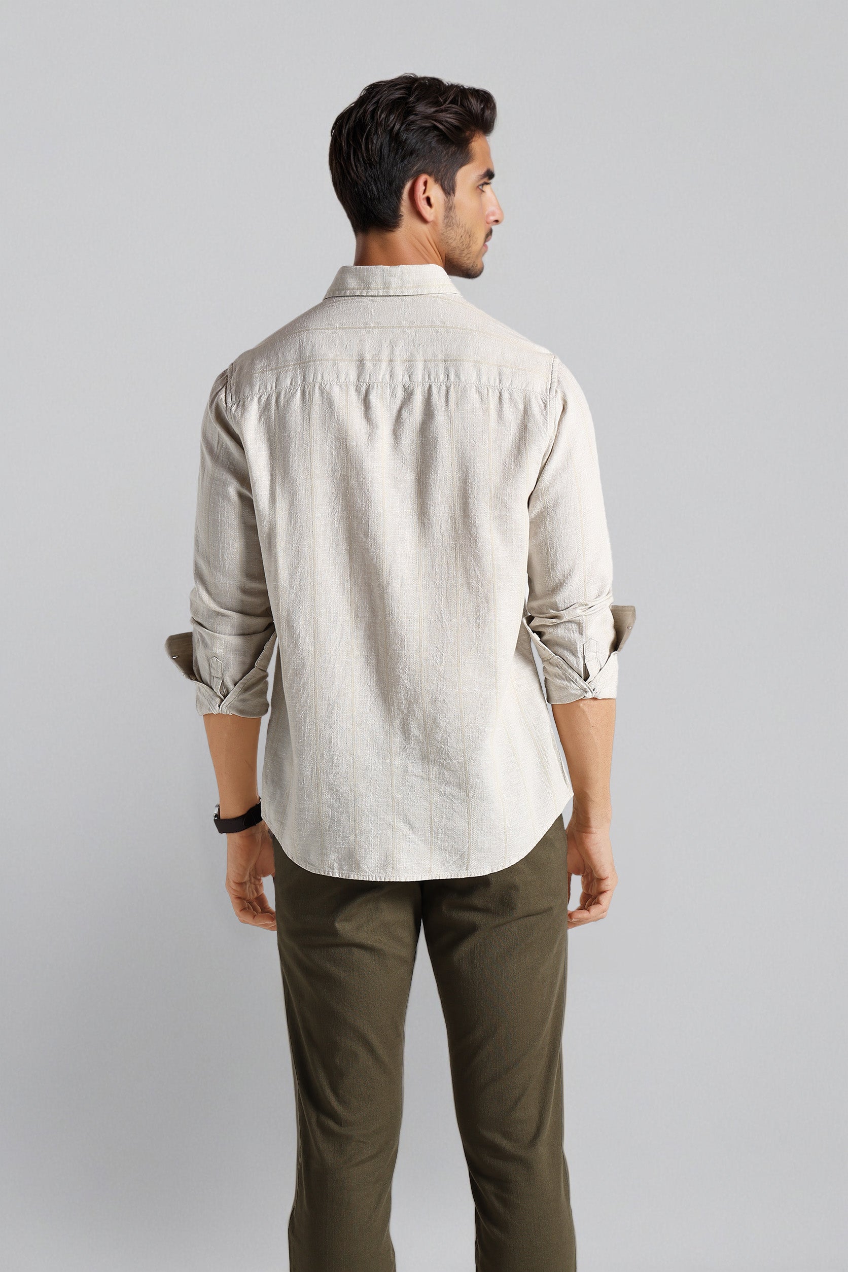 Man wearing a light-colored shirt and dark pants against a plain background