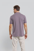 Man wearing a striped polo shirt and light-colored pants on a plain background