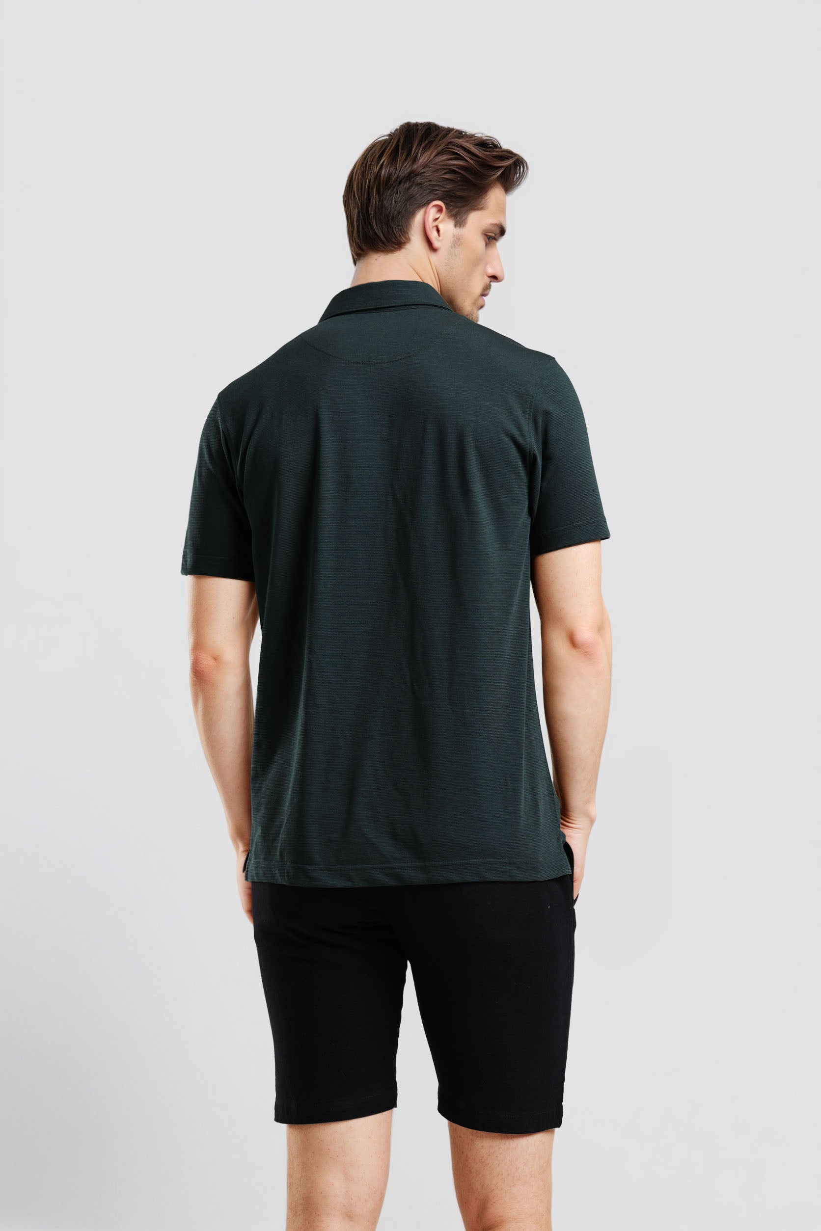 Man wearing a dark green polo shirt and black shorts on a light gray background