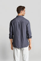 Man wearing a dark gray button-up shirt and white pants on a light gray background