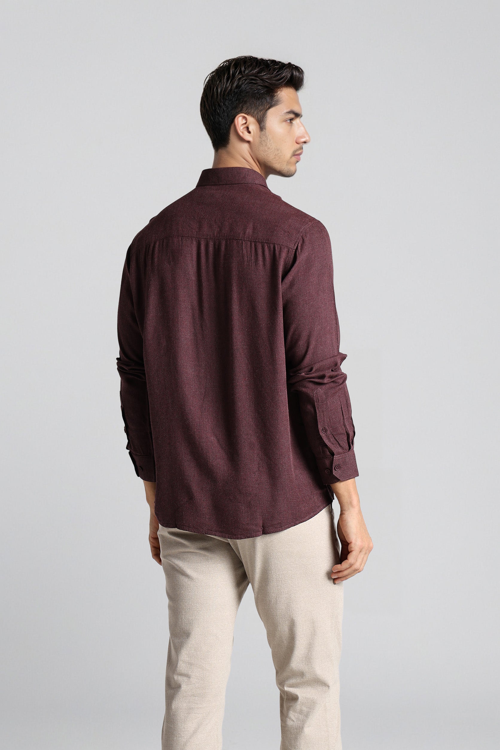 Man wearing a maroon shirt and beige pants on a light gray background