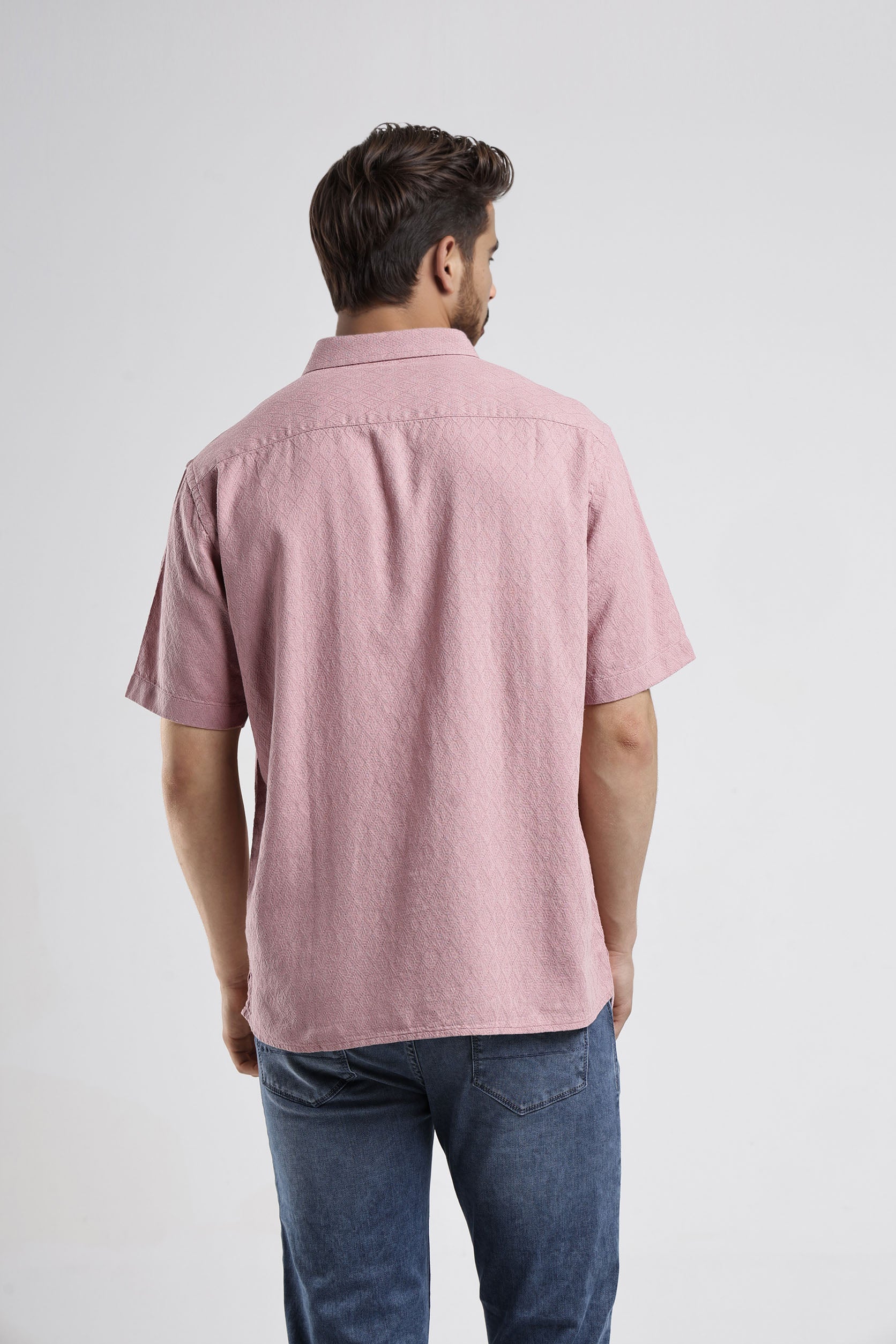 Man wearing a pink short-sleeve shirt and blue jeans on a white background