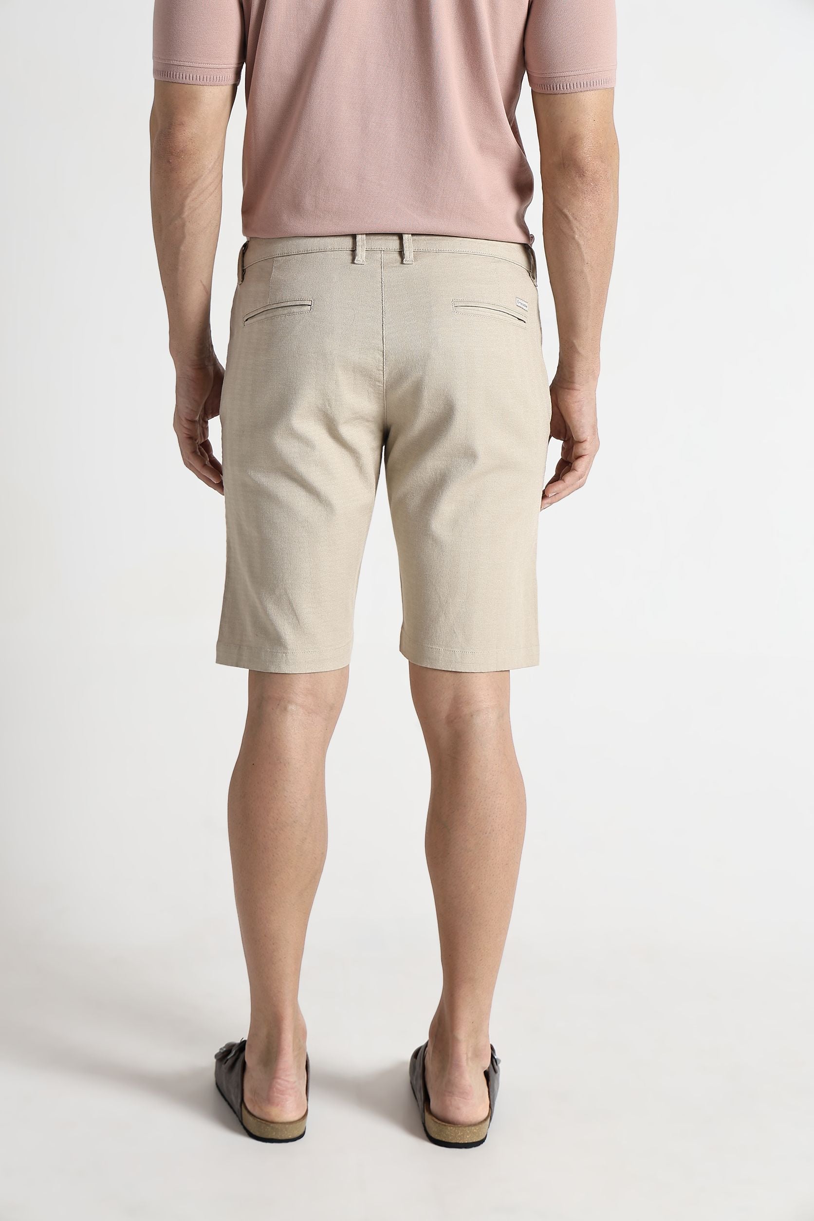 Person wearing beige shorts and a pink shirt on a white background