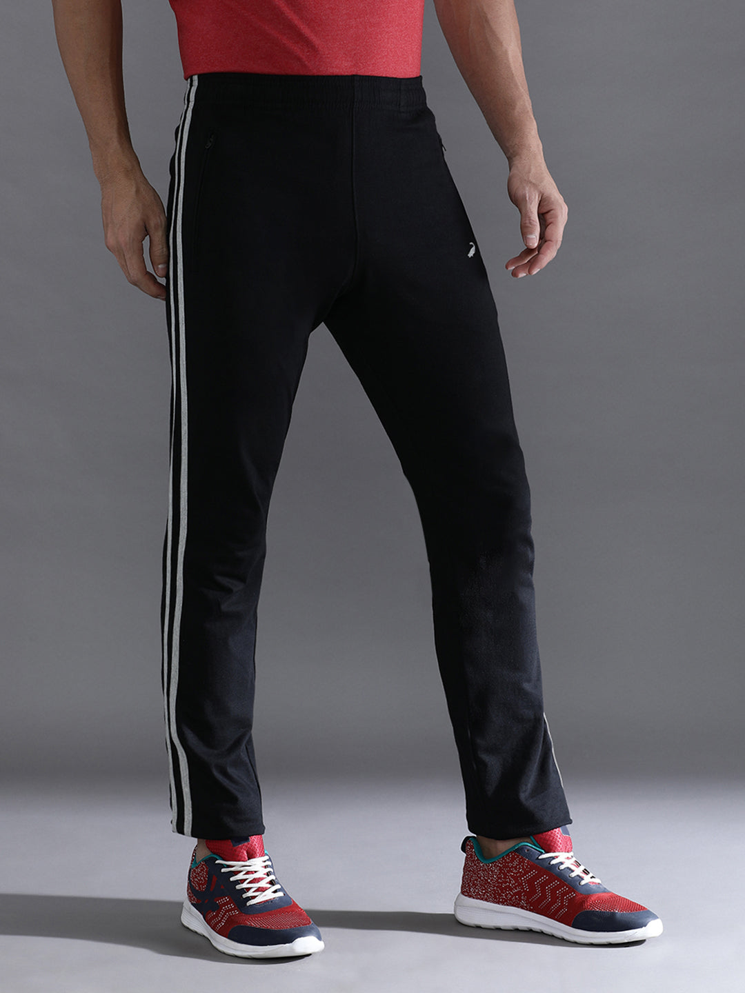 Person wearing black pants with white stripes and red sneakers on a gray background