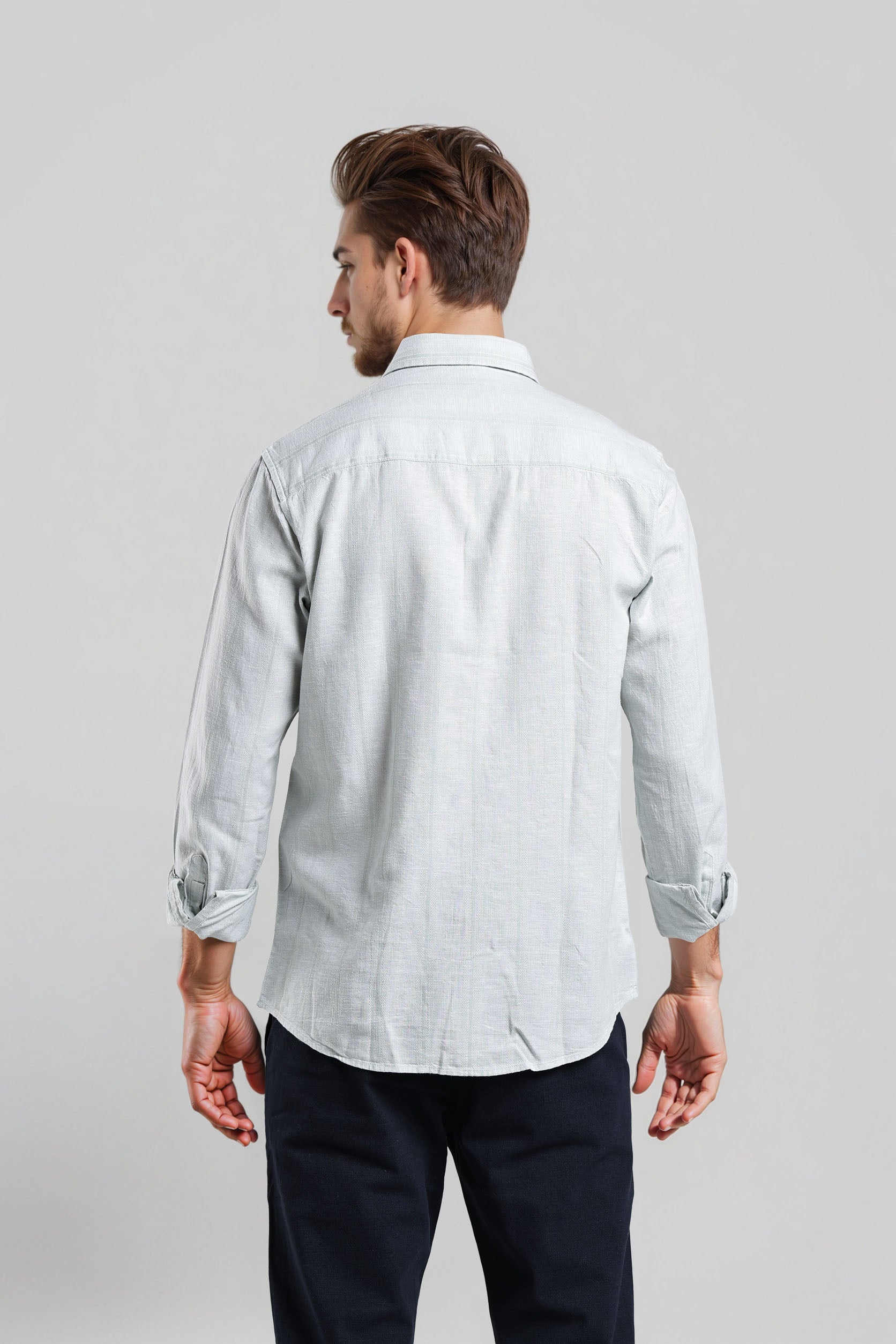 Man wearing a light-colored shirt with rolled-up sleeves on a plain background