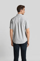 Man wearing a gray checkered shirt and dark pants on a light gray background