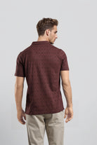 Man wearing a maroon patterned polo shirt on a light gray background