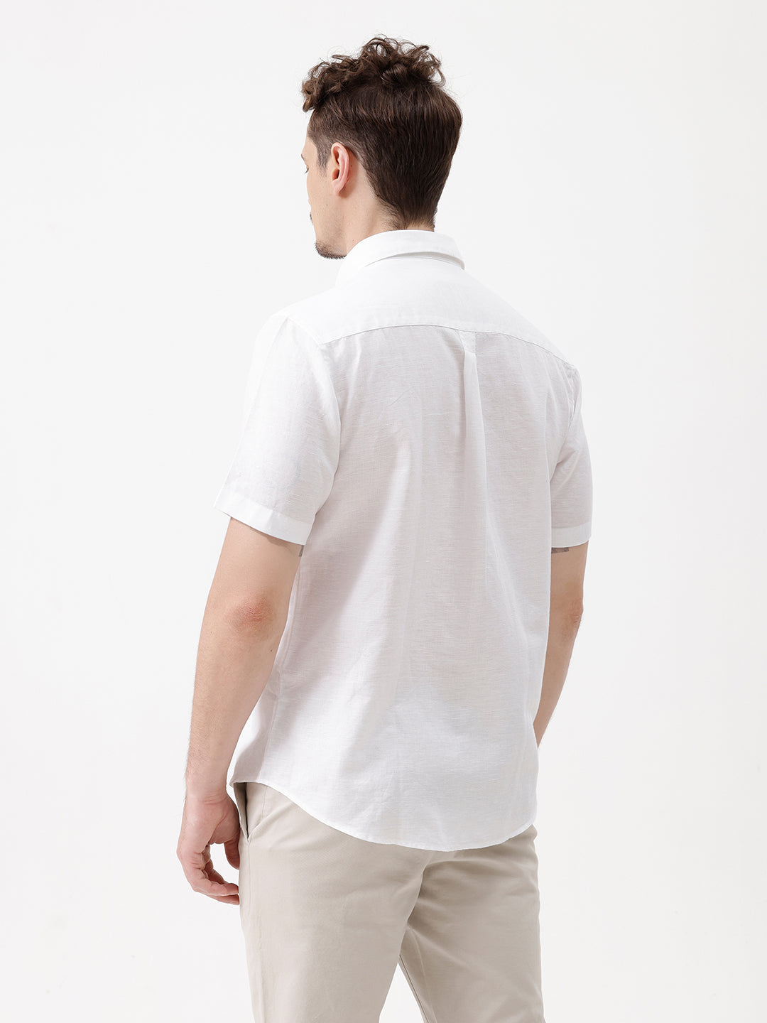 A man wearing a white short-sleeve button-up shirt with a chest pocket and beige trousers, standing against a plain white studio background.