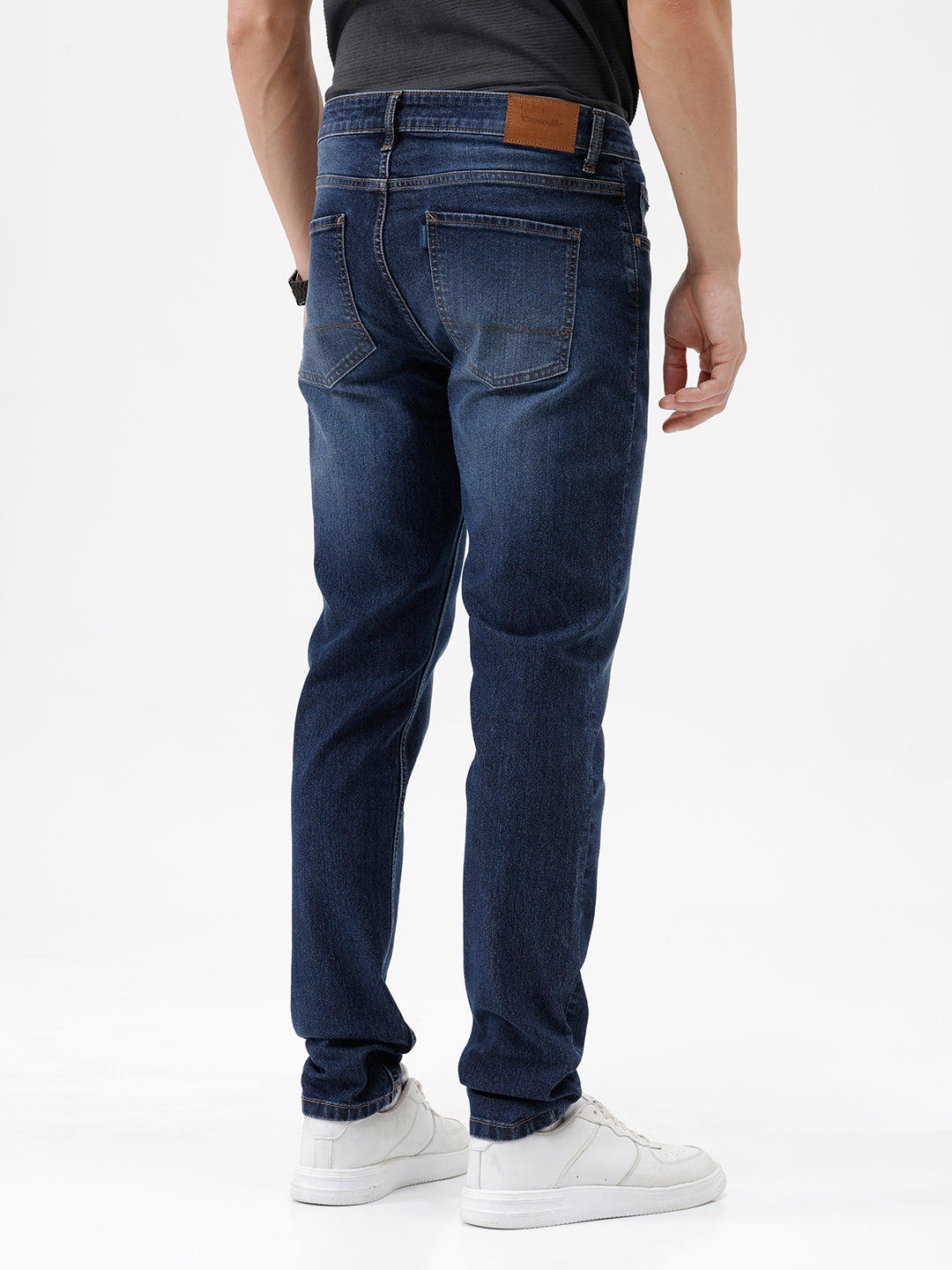A person wearing dark blue slim-fit jeans with a faded wash, paired with a black t-shirt and white sneakers, shown from the waist down against a plain white studio background.