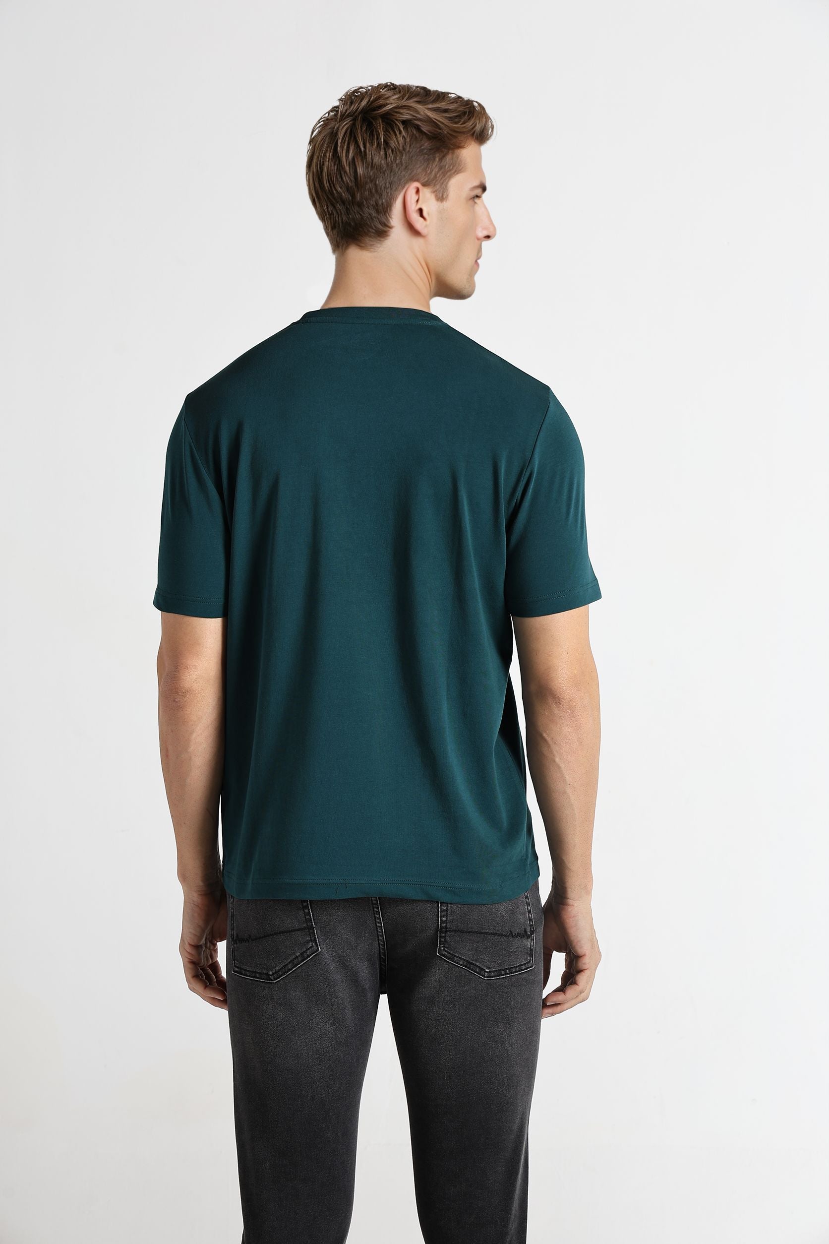 Man wearing a teal t-shirt and dark jeans on a white background