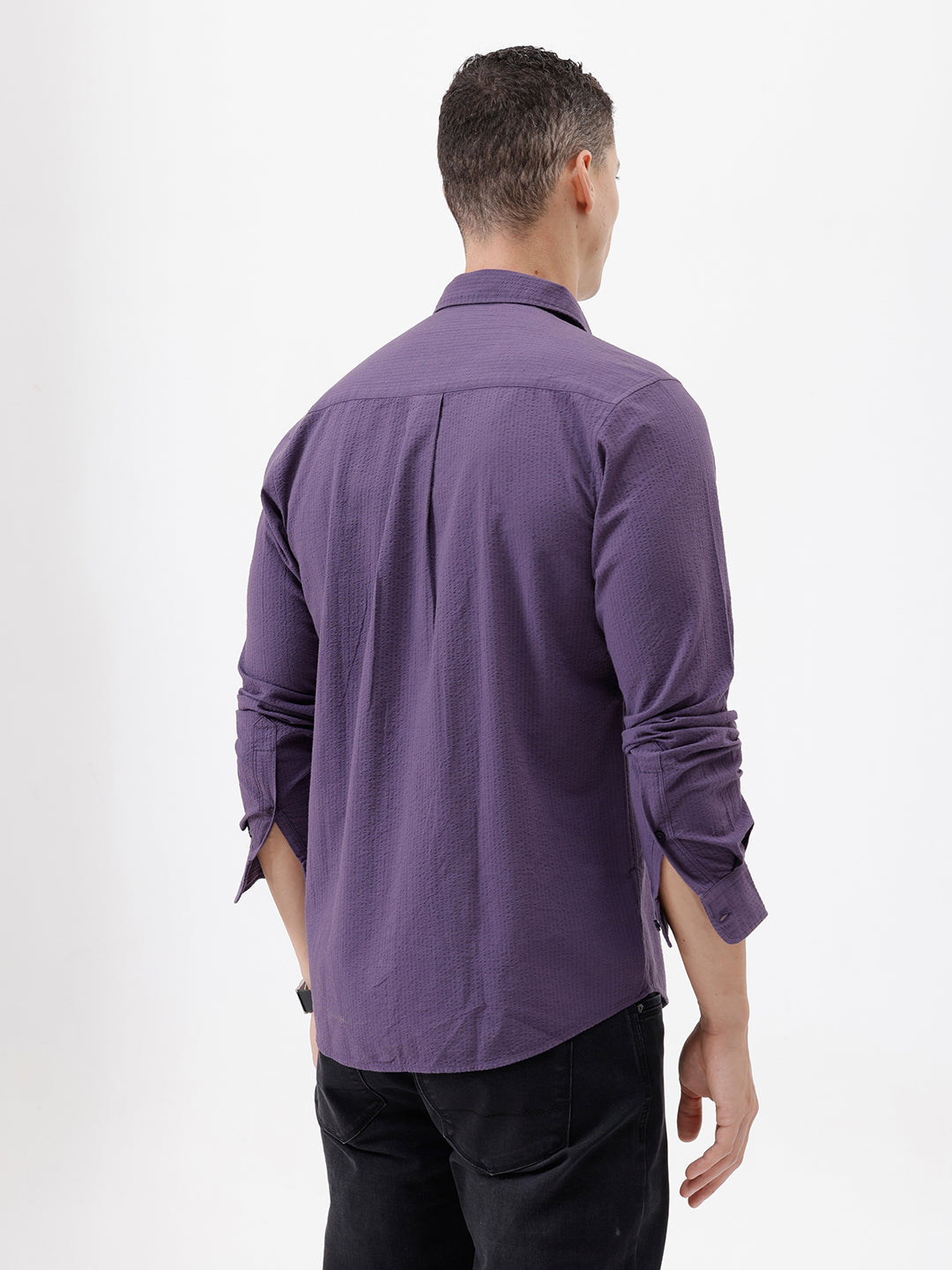 A man wearing a long-sleeve button-down shirt in a muted purple color, paired with black pants, standing against a plain white studio background.