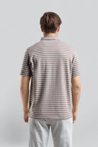 Man wearing a striped polo shirt and light pants against a plain background