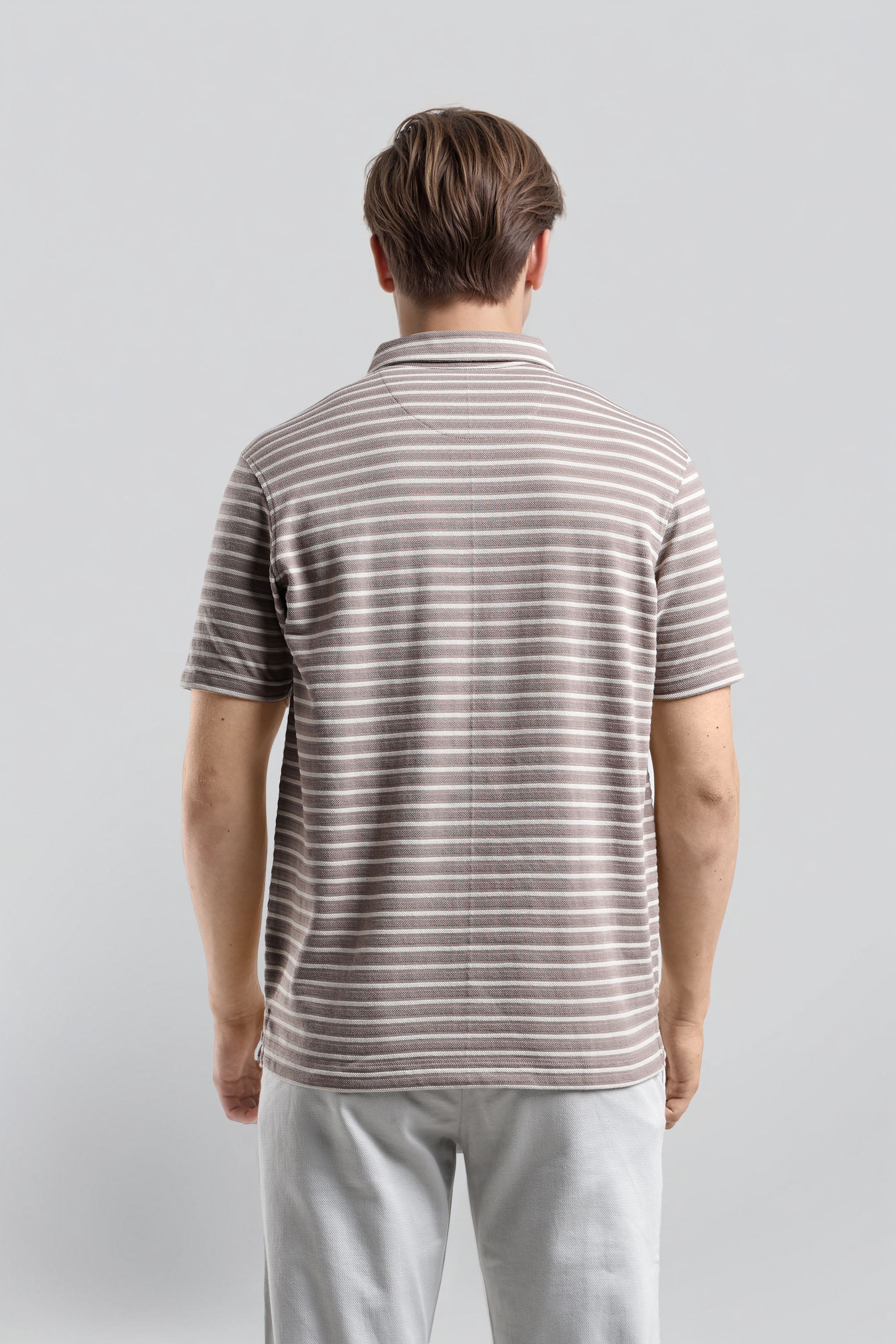 Man wearing a striped polo shirt and light pants against a plain background